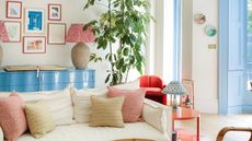 colorful living room with blue console, patterned cushions and gallery wall of colorful artwork, cream sofa and blue shutters