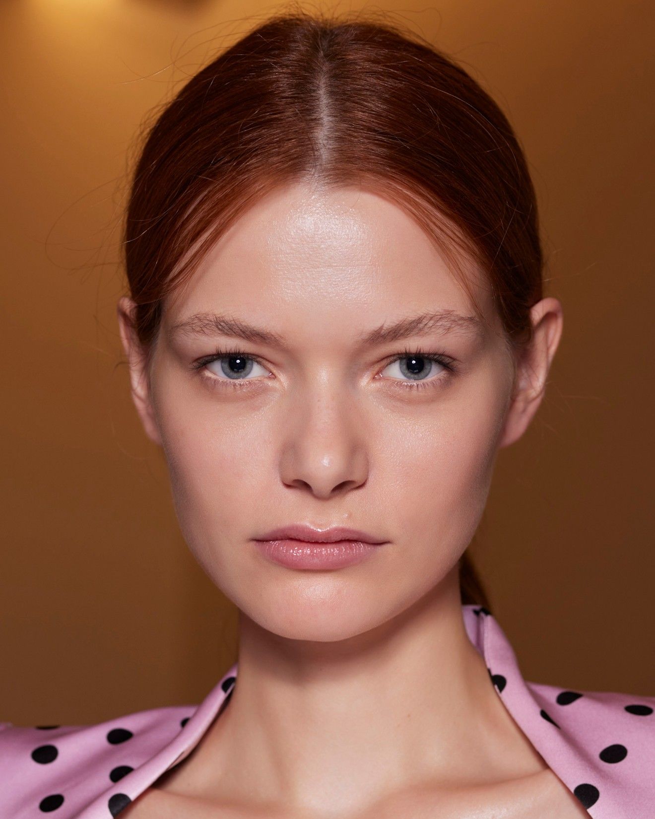 A model with red hair and a center part in a pink polka dot shirt