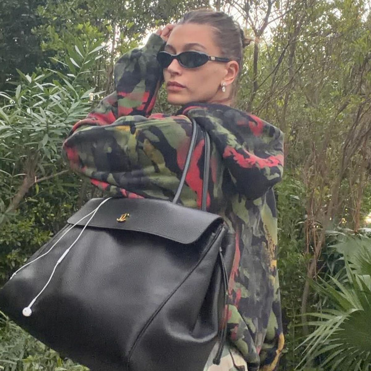Hailey bieber wears a camouflage sweatshirt and a black tote bag.