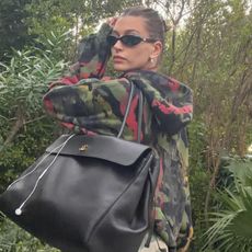 Hailey bieber wears a camouflage sweatshirt and a black tote bag.