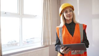 female building surveyor in house with clipboard