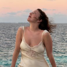 A photo of @emmahoareau by the sea wearing a cream dress