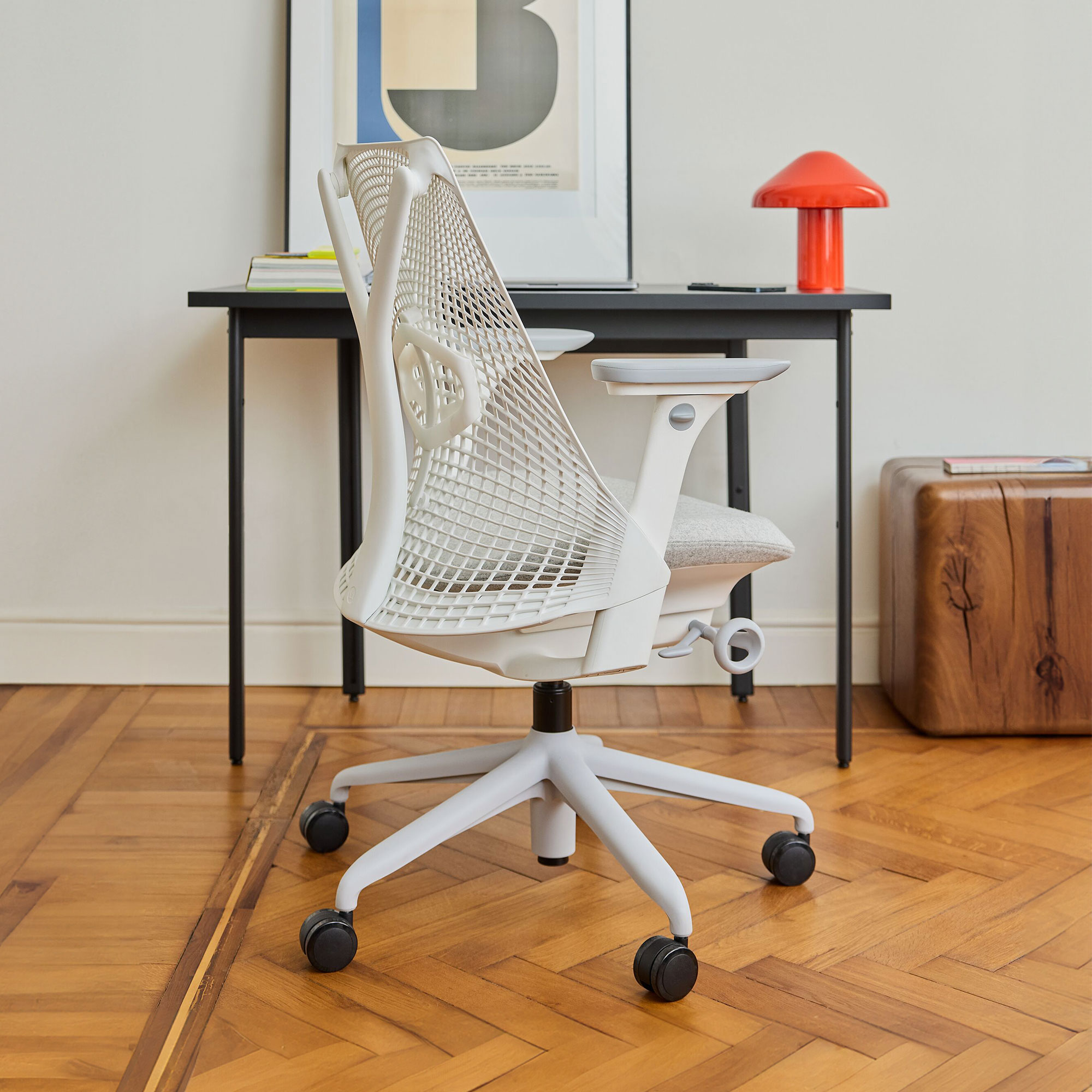 White office chair at dark grey desk with orange wireless lamp and oversized graphic print in thin frame
