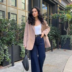 Influencer @kristincabat wears dark wash flared jeans with pointed toe boots and a camel blazer.