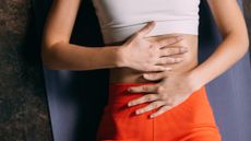 Woman in sportswear lies on her back on a yoga mat, with her hands over her midsection