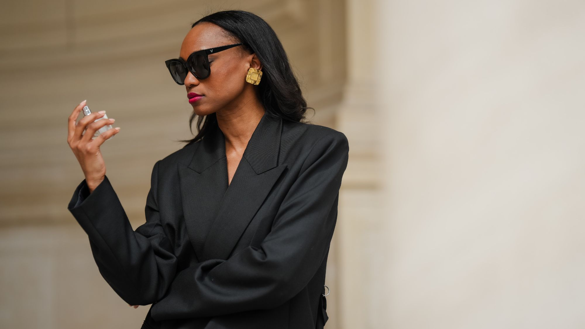 street style shot of a woman in a black blazer holding a perfume bottle