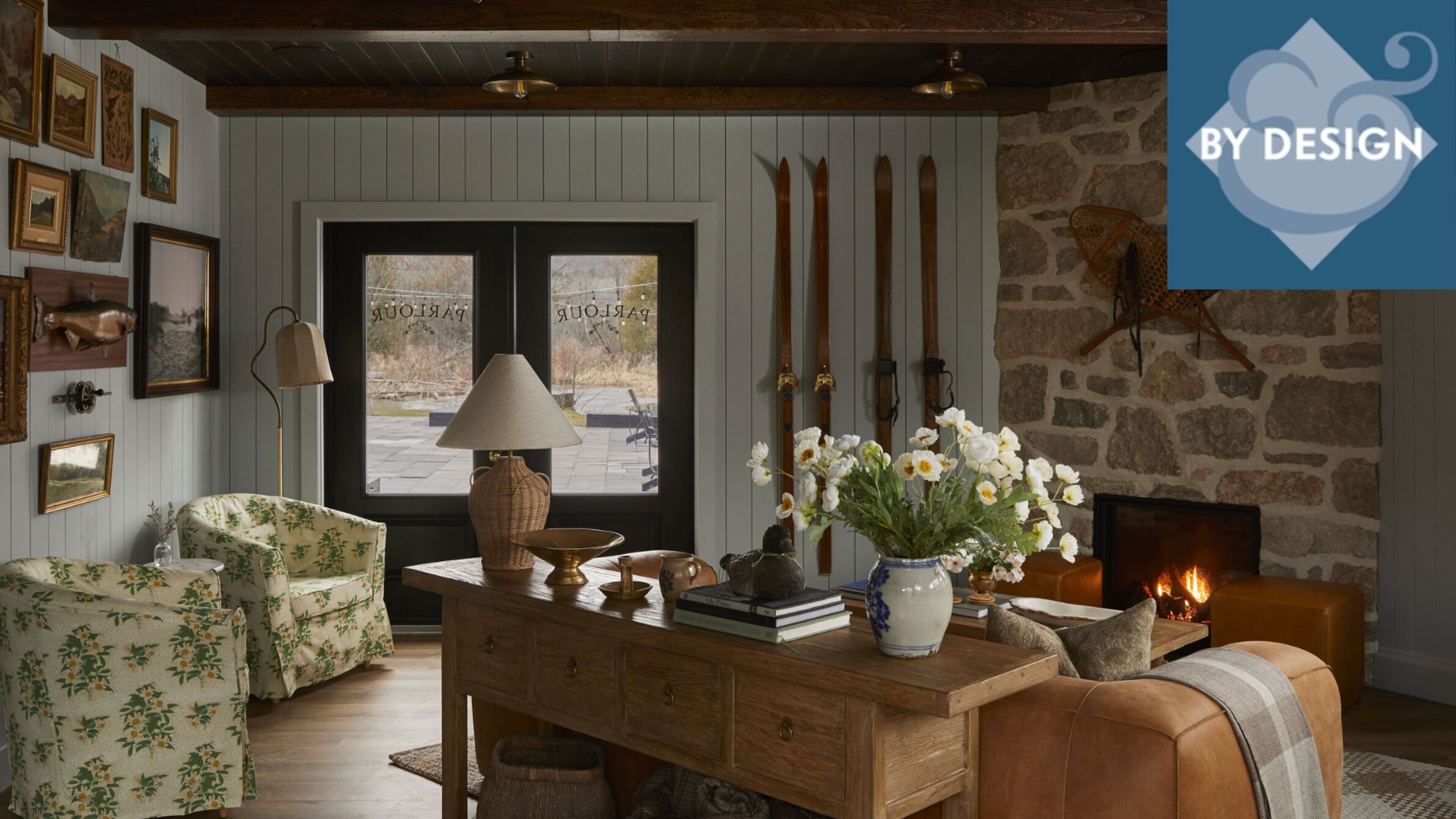 Cozy entryway with brick and panelled wood wall, gallery wall, two patterned armchairs, wooden console table decorated with ornaments, firepplace 