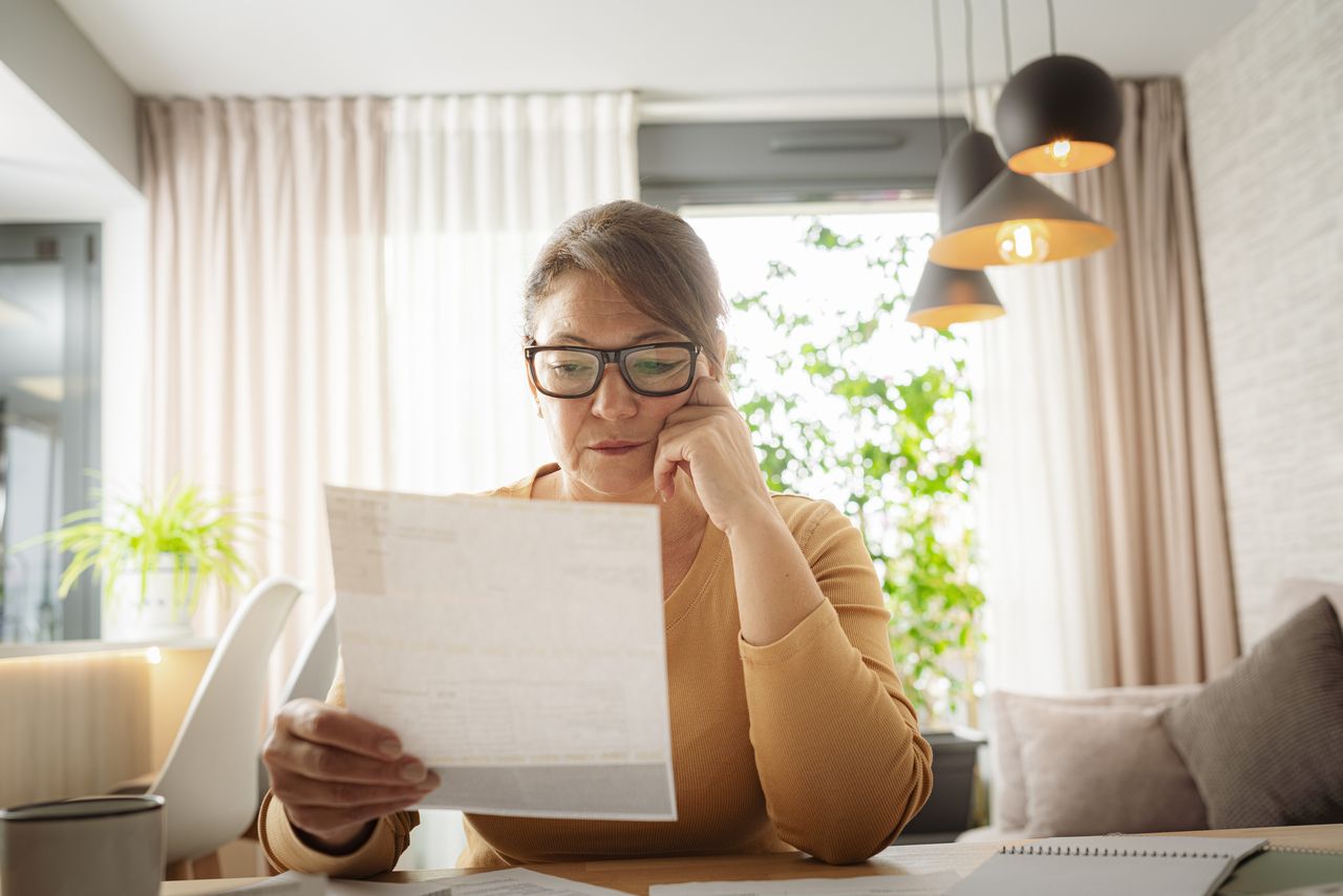 Woman reads payslip as she sits at kitchen table.