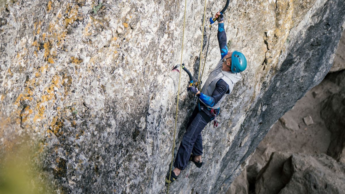 Drytooling man holding special equipment for climbing in blue helmet climbs an overhanging rock