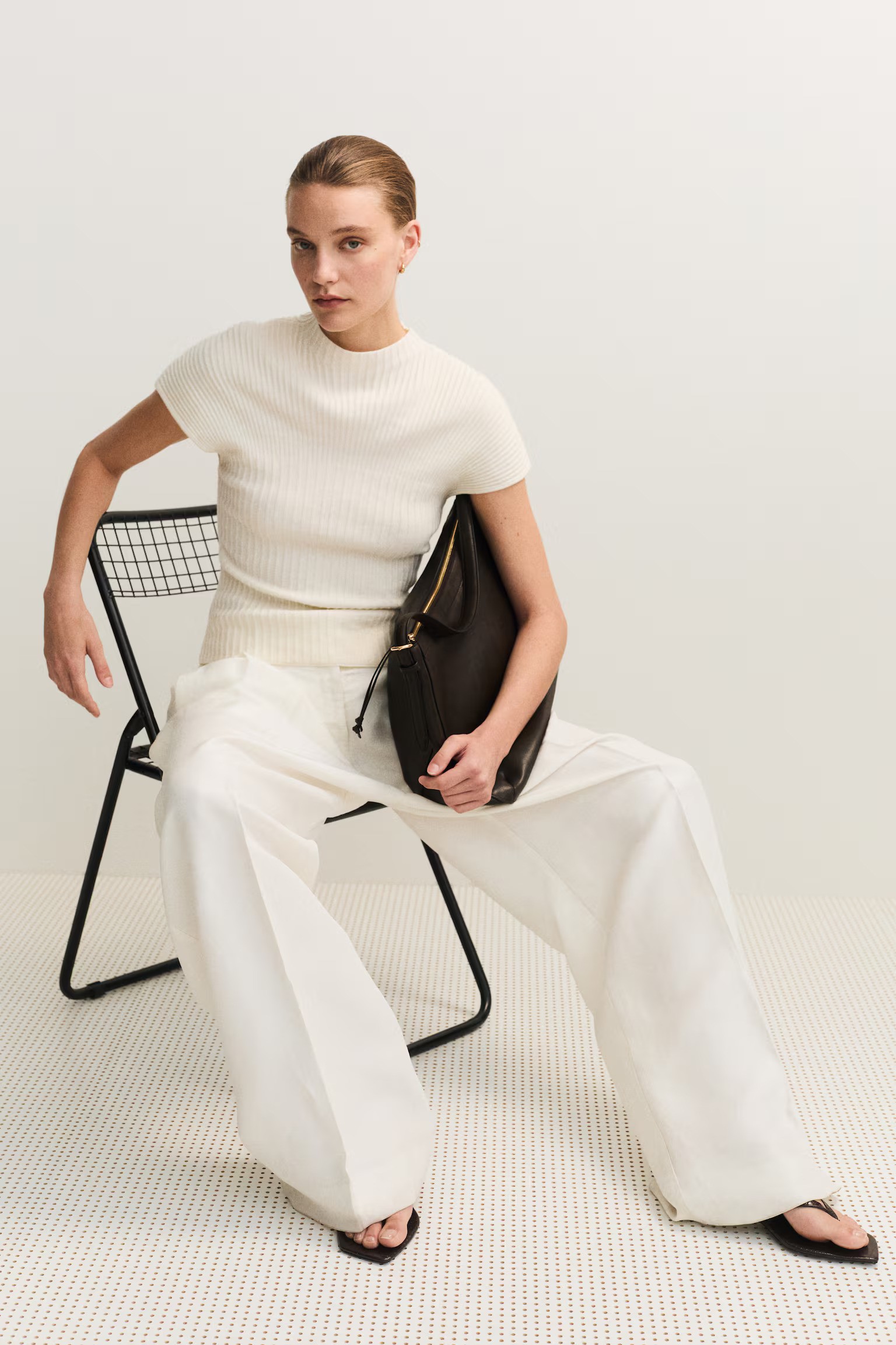 Model wears cream knit top, cream tailored trousers and black sandals