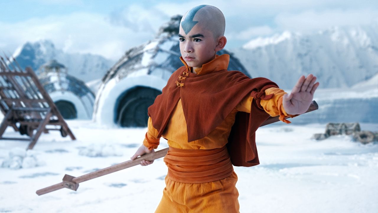 a bald-headed boy (Gordon Cormier as Aang) thrusts out his hand while holding a wooden staff and standing in front of an igloo, in episode 101 of Avatar: The Last Airbender