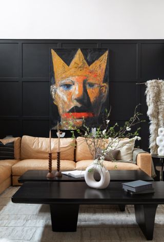 Living room with black panelling against white wall, tan sofa and black coffee table