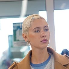 Iris Law wearing a tan coat, gray cardigan, beige jeans, blue sneakers, and a lime Louis Vuitton speedy bag