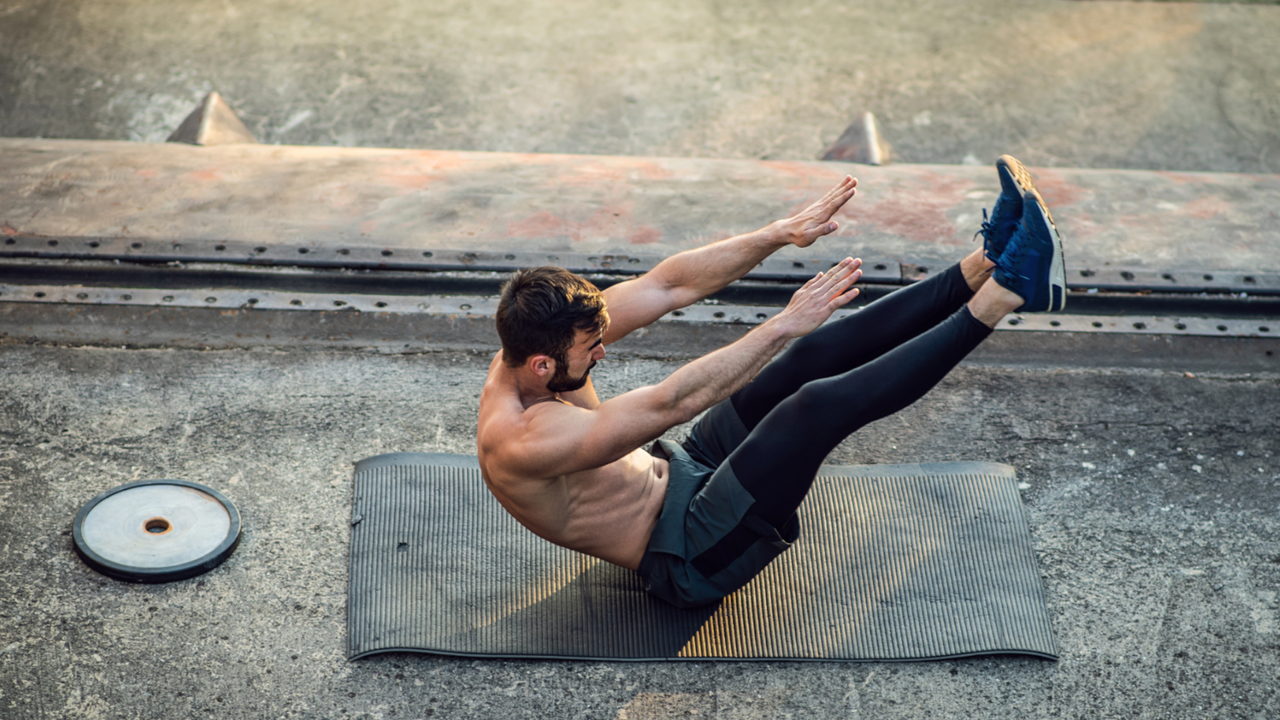 A man performing V sit ups on a exercise mat outside