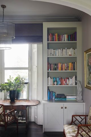 Living room with neutral walls and bookshelves with cupboards below, armchair, side table and chair