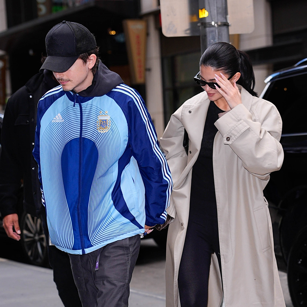 Kylie Jenner wearing a trench coat, black tee, black capri pants, and black thong sandals