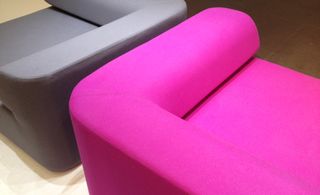 light wood floor, close up of a bright pink upholstered chunky armchair next to a grey chair of the same design