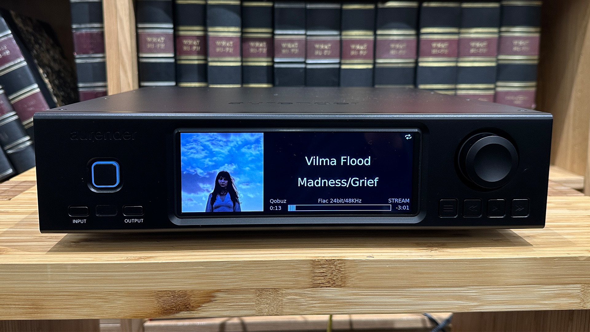 Aurender A1000 music streamer on wooden hi-fi rack in front of bookcase