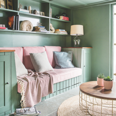 Built in sofa with green walls, cupboards and ceiling, pink cushions and grey tiled floor. Rachel and Manuel Noguiera's renovated four bedroom family home, a detached thatched 16th century listed cottage in Crantock, Cornwall.