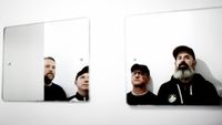 A photo taken in the mirror of the four members of the band Mogwai. Three of them are wearing hats.