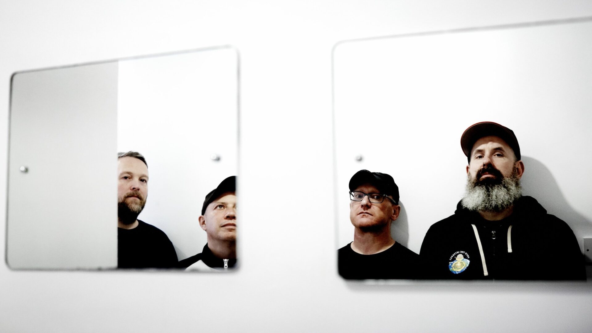 A photo taken in the mirror of the four members of the band Mogwai. Three of them are wearing hats.