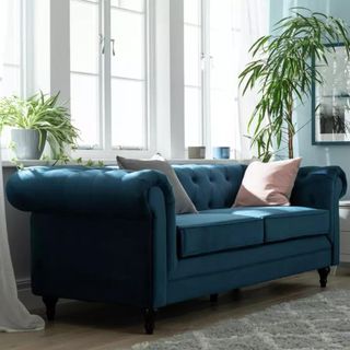A blue chesterfield sofa in front of a living room window