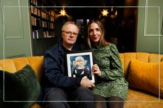 Jason Watkins and wife Clara Francis sat on an orange sofa holding a photo frame with a picture of their daughter Maude