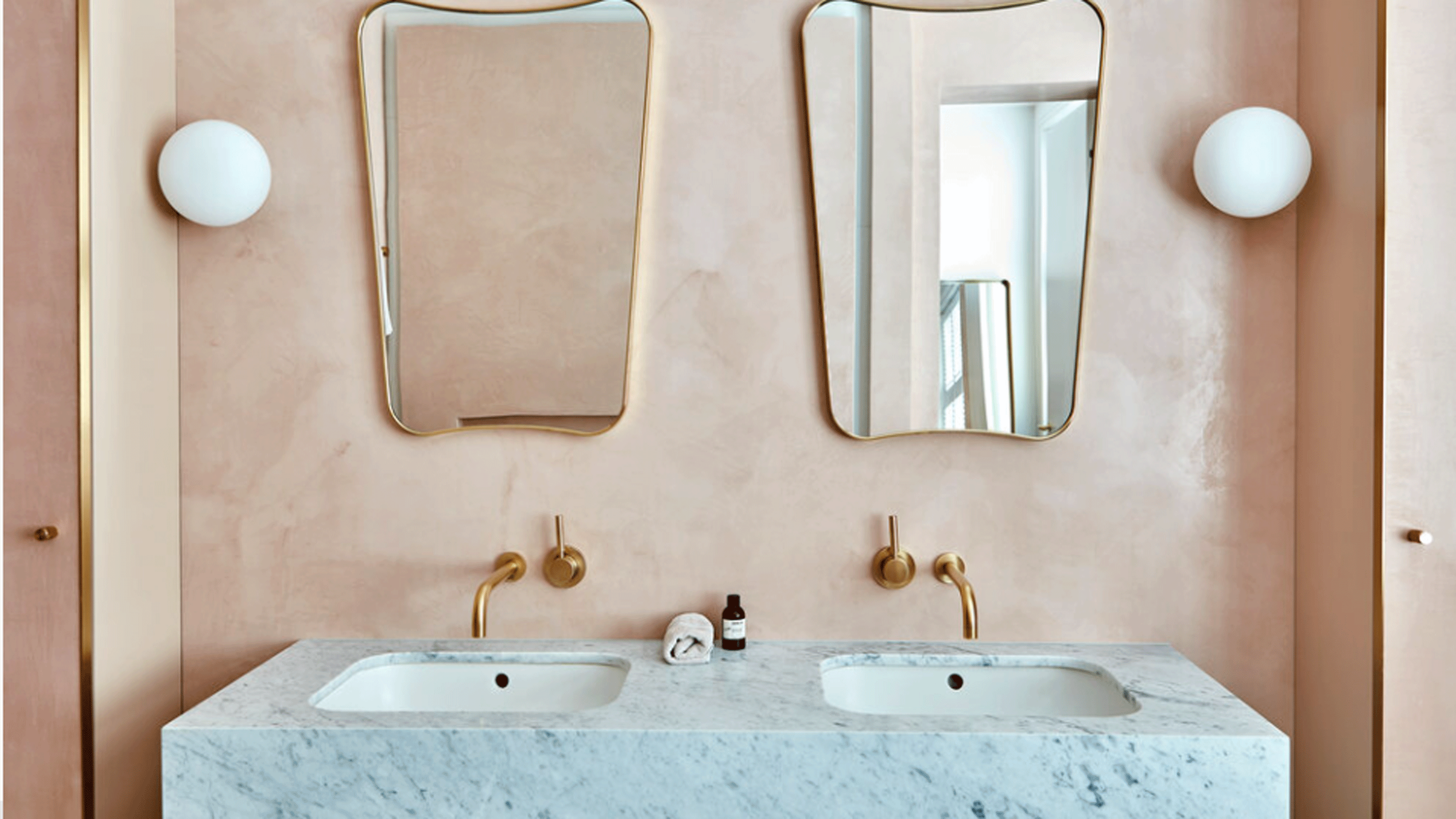 Pink tadelakt bathroom walls with two shield mirrors and double sinks