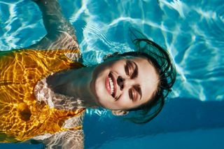 Beautiful girl in a yellow swimsuit swims in the pool and smiling