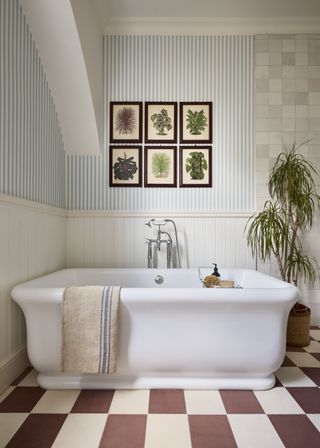 bathroom with blue stripe wallpaper, white tub shower, artwork, plant, checked floor tiles