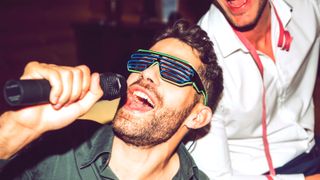 Close-up of young man singing karaoke while enjoying with friends in party.