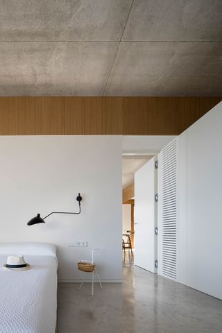 Minimalist bedroom with white walls and bedding, concrete floors and a black lamp at Port de la Selva house
