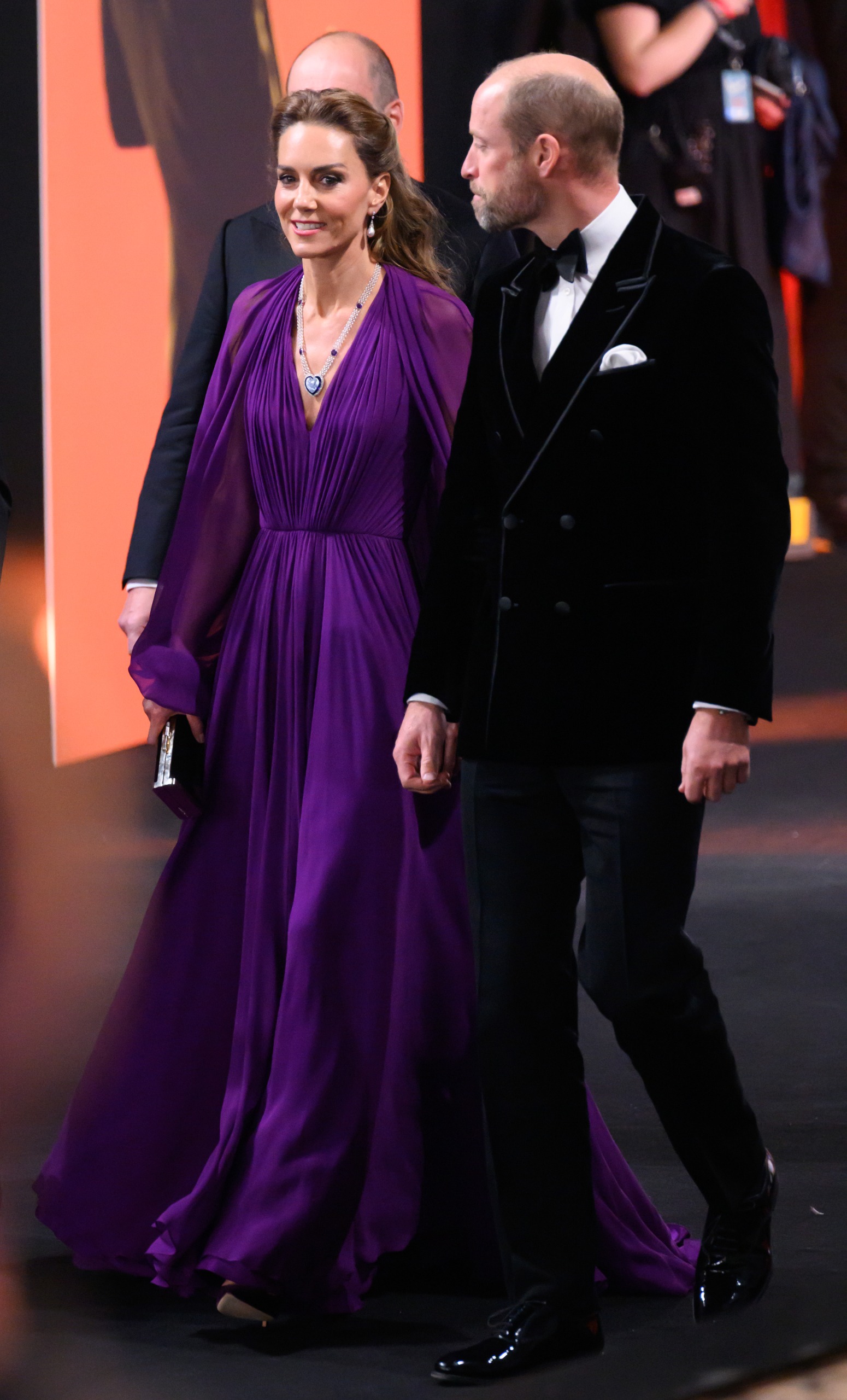 Kate Middleton arrives at the "Digger" Premiere wearing a royal purple long-sleeve maxi dress with a long necklace and drop earrings. She walks alongside Prince William.