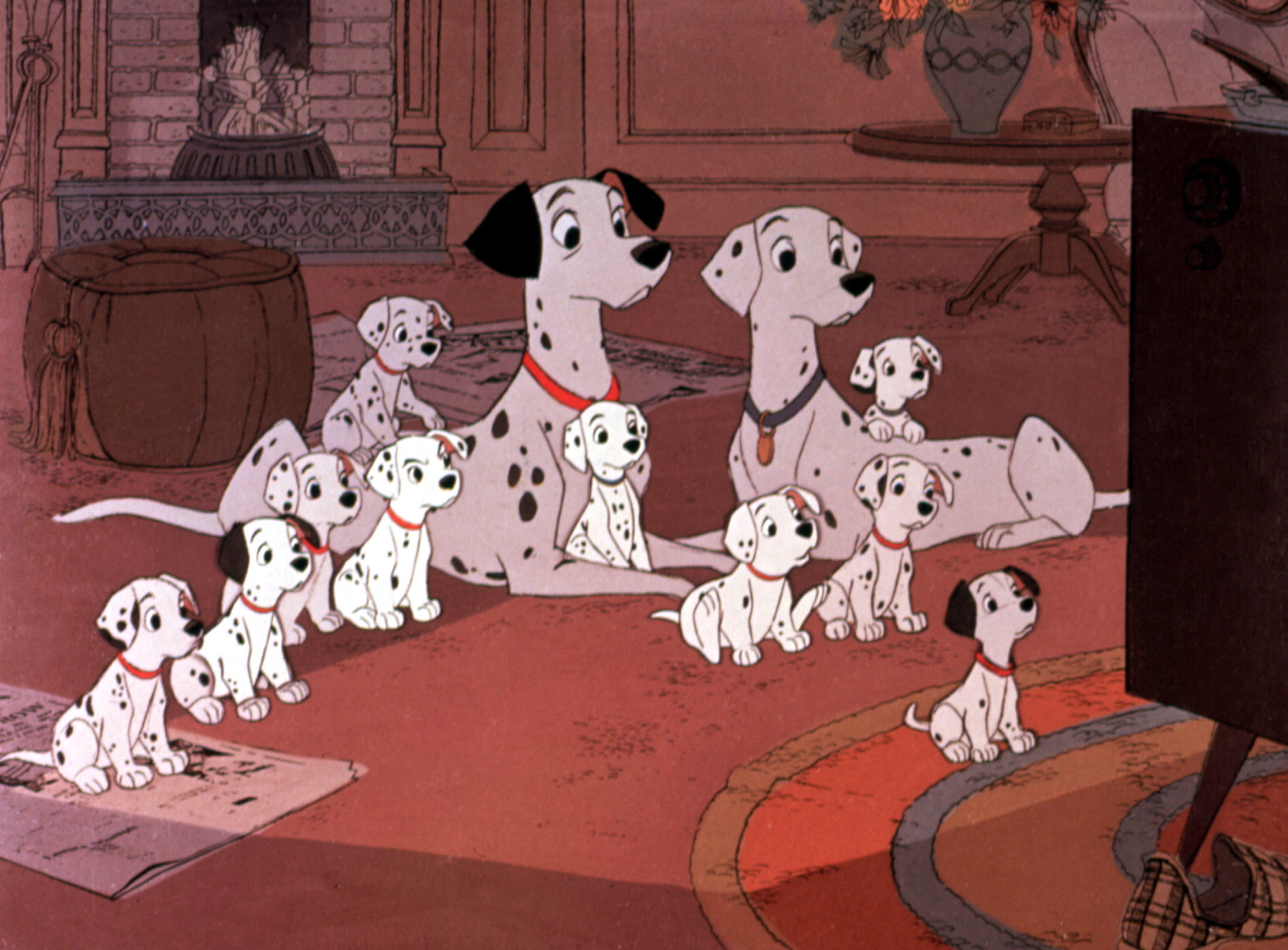 An animated scene from 101 Dalmatians showing two adult dalmatians and their puppies sitting together in a living room, all facing a television set just out of frame.