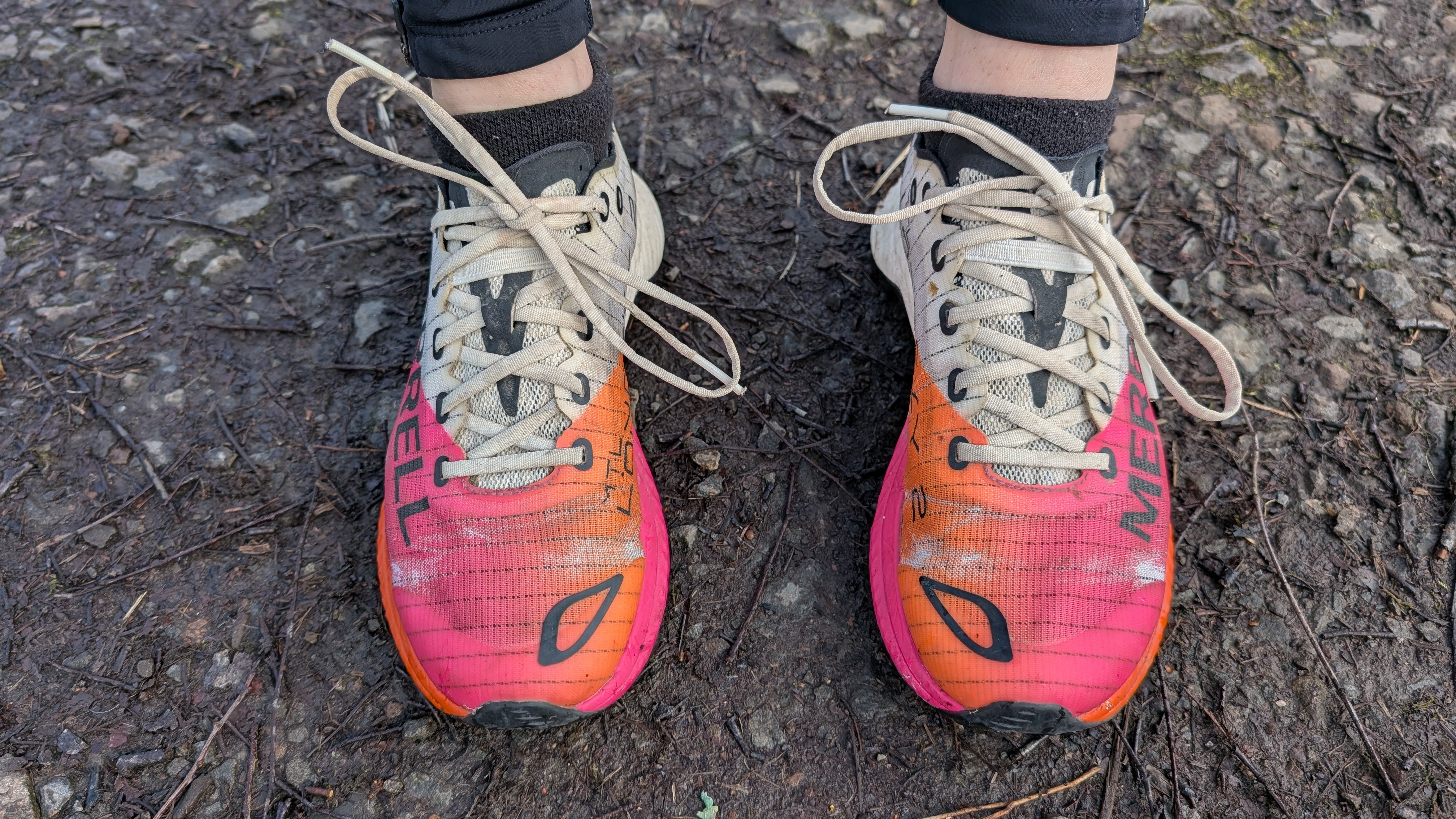 A runner's feet wearing pink and orange Merrell MTL Long Sky 2 trail running shoes