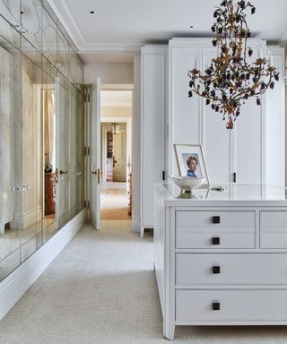 A bedroom furniture idea with dressing area with mirrored wardrobes, white island and black chandelier
