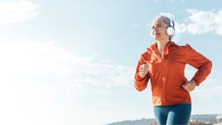 Woman running along beachfront in headphones and jacket