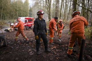 Eve watching a Three Rock camper shovel to her right, three more campers are standing behind her shovling dirt.