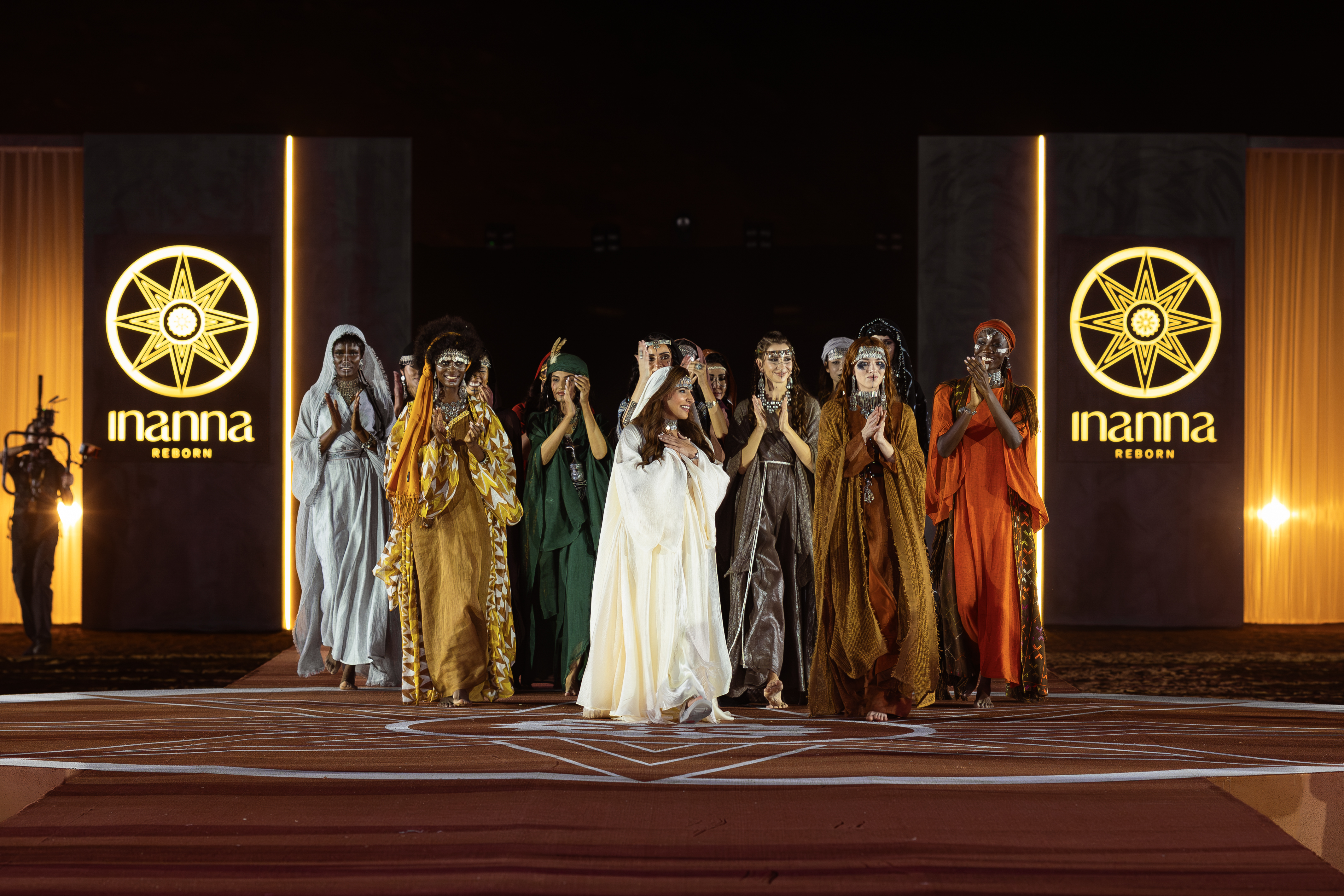 Runway models clapping on a stage with lit up signs saying Inanna Reborn