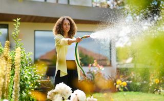 A woman waters a lawn and flowerbed with a hosepipe 