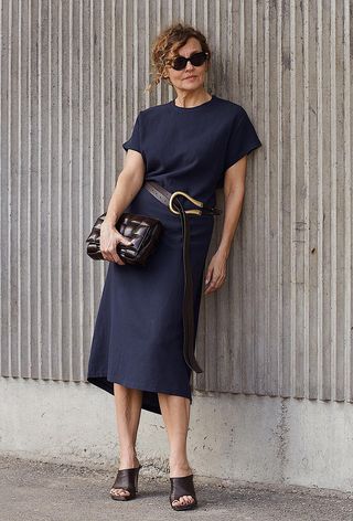 a photo showing what to wear to the office in the summer with a woman wearing a navy blue crewneck midi dress with a brown belt, brown mules, and a brown handbag