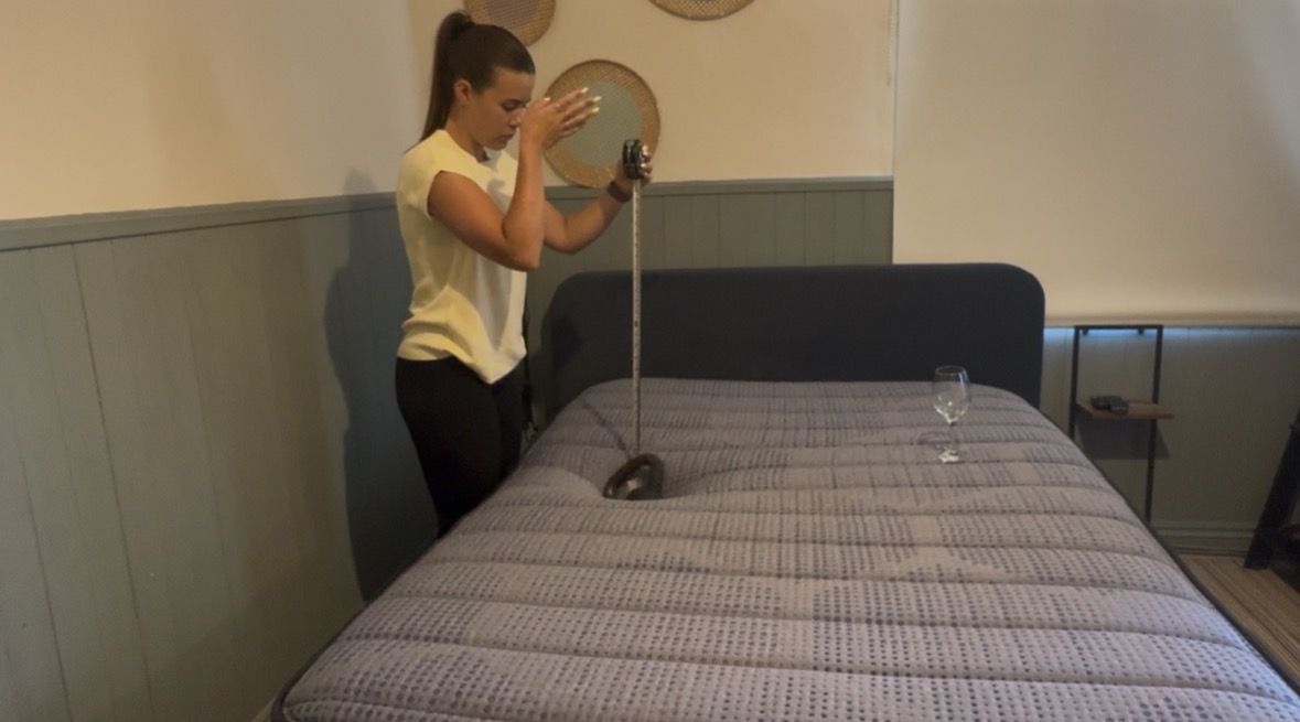 Our mattress tester performing objective motion isolation tests on Brooklyn Bedding Copperflex Memory Foam Mattress. Wearing a yellow top, she drops a kettlebell on to the left hand side of the bed with a wine glass standing on the other side.
