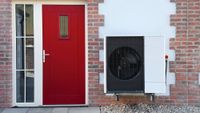 red front door on brick and rendered wall with heat pump mounted on wall beside door