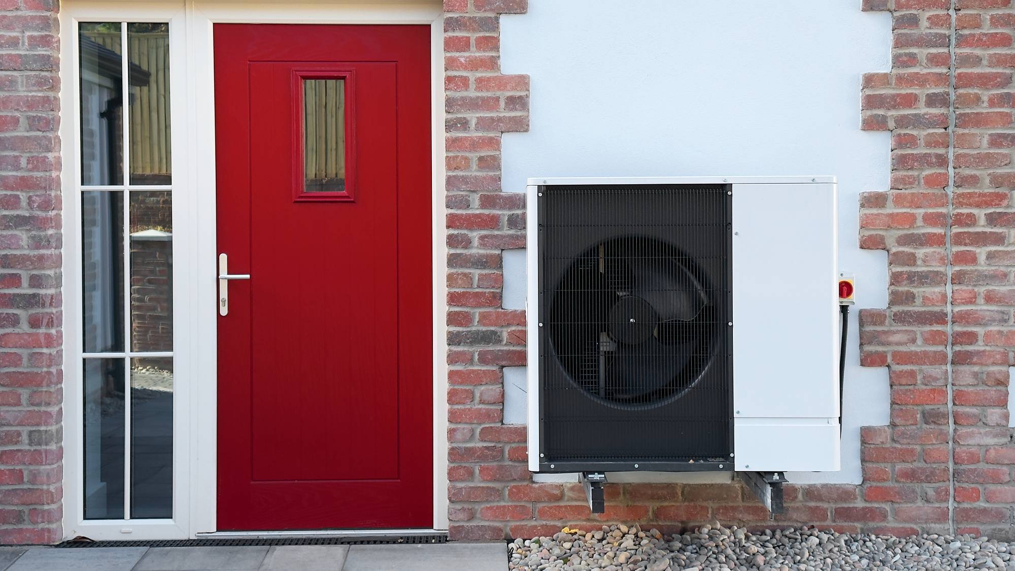 red front door on brick and rendered wall with heat pump mounted on wall beside door