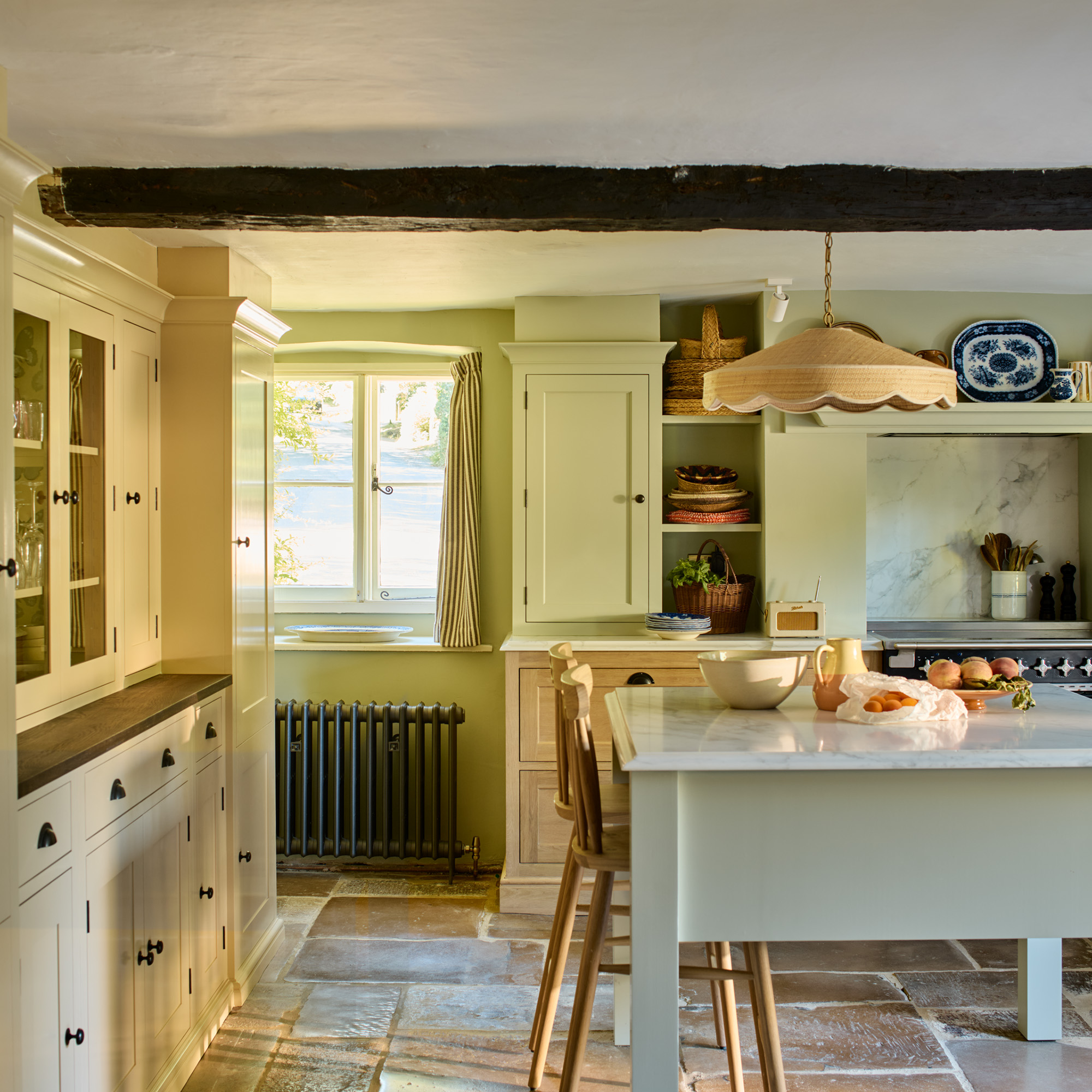 country kitchen with cream and oak cabinetry and sage island with flagstone floor and wooden bar stools