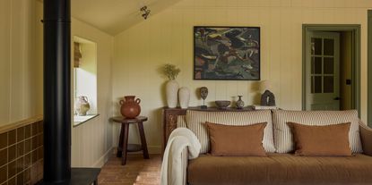 A warmly furnished farmhouse boasts an earthy palette of browns, greens, and ochres along with sculptural crafty pieces, including ceramics, patterned fabrics, and original artwork.