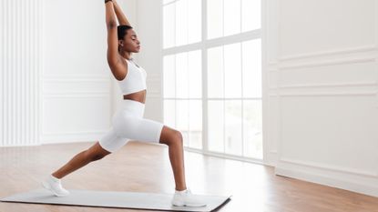 A woman performing a bodyweight lunge with overhead reach