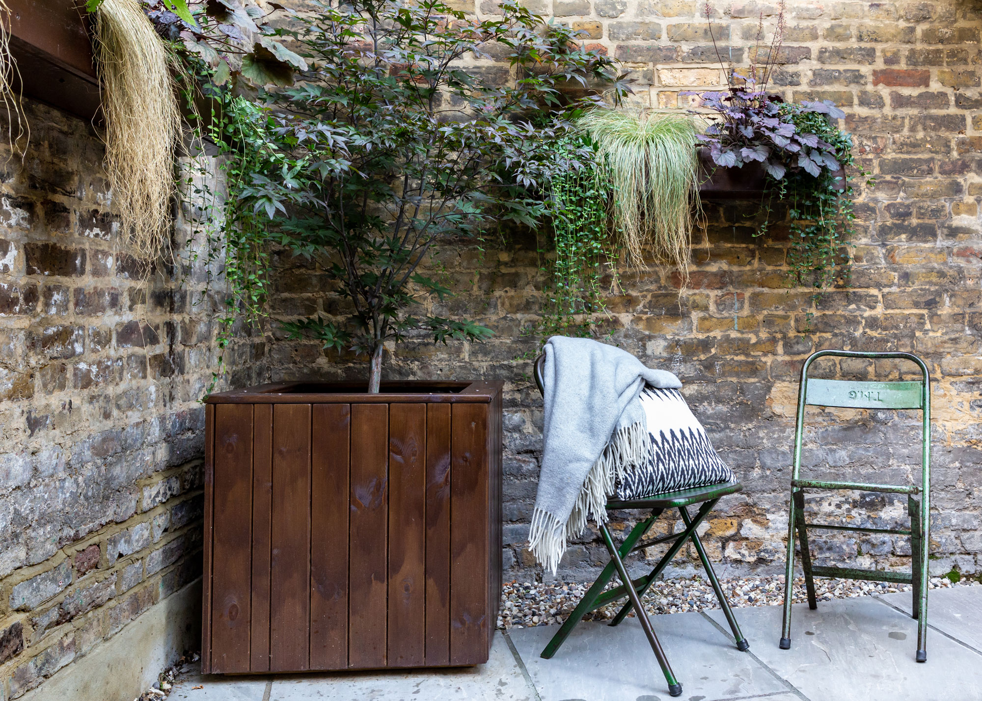 acer tree in corten planter with bistro chairs, brick wall and tough planters with trailing plants