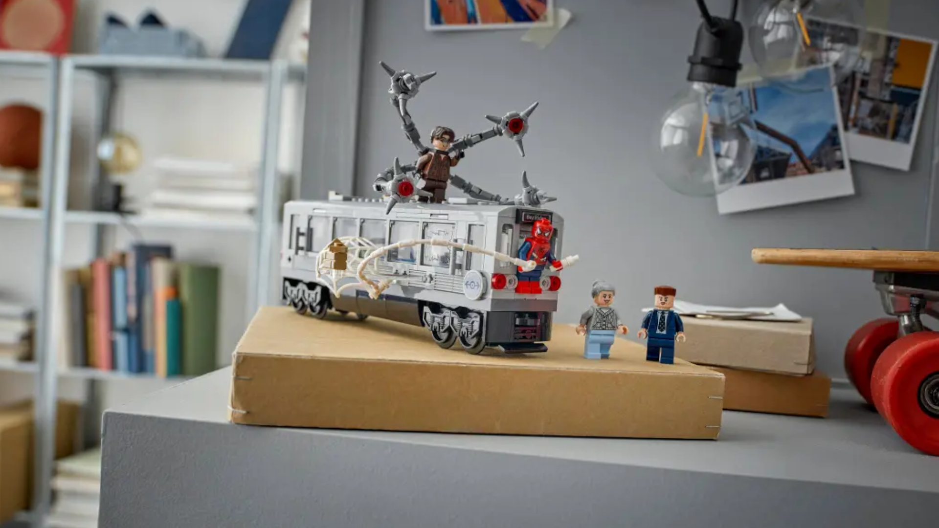 A Lego train with Spider-Man on the front, two minifigures to one side, and Doc Ock up top on a cardboard box and gray surface with Polaroid photos nearby