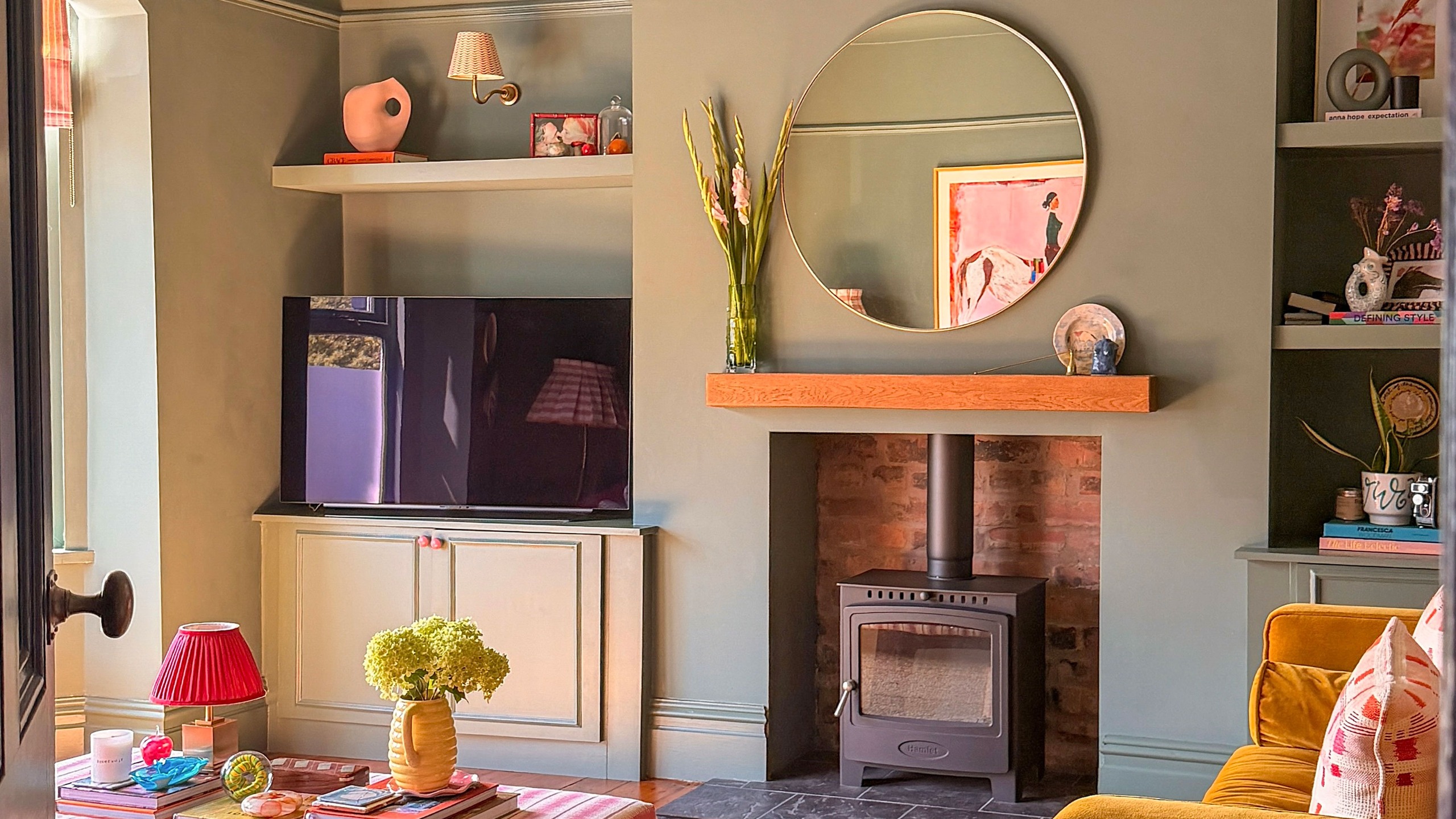 Sage green living room wood burner and round wall mirror